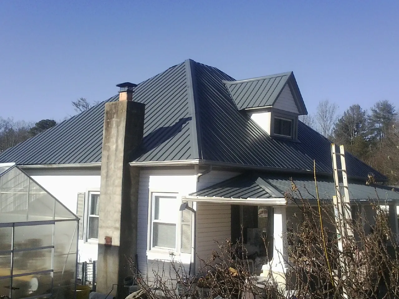 Dark blue standing seam metal roof on a white farmhouse with dormer — Slate & Tile Roof Repair by Roofing Brothers in White
