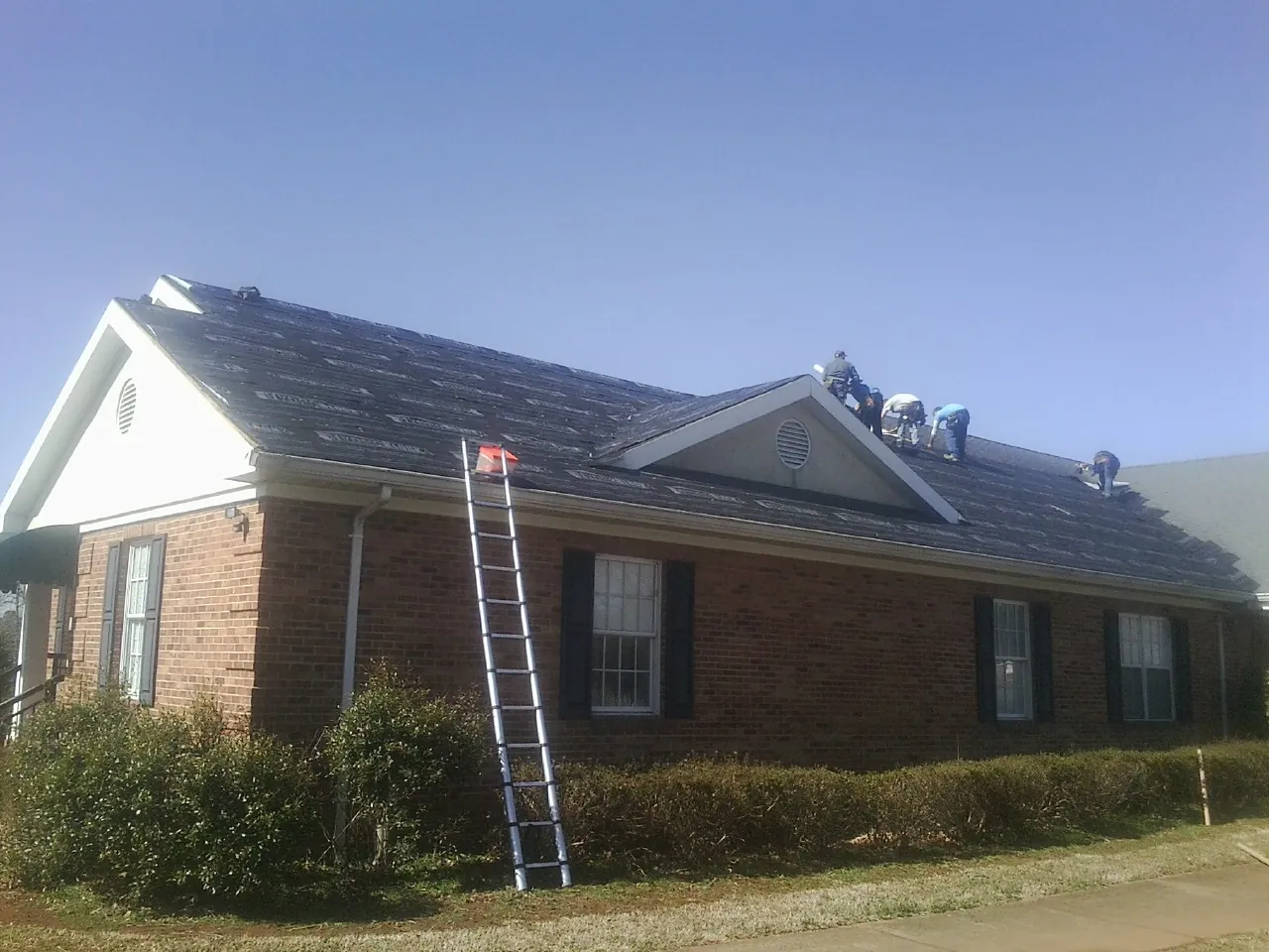 Crew tearing shingles off a brick ranch roof with a ladder set — Metal Roof Repair work by our crew in White
