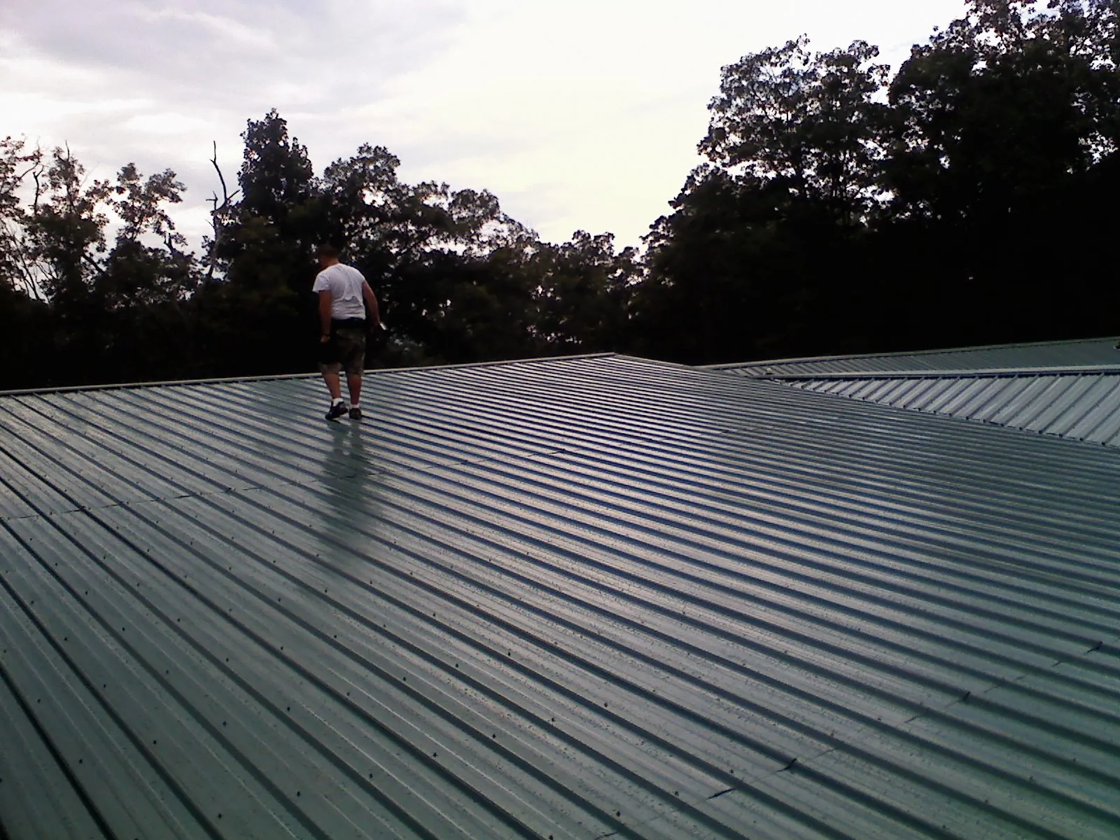 Roofer walking a wide expanse of new green metal roofing in White